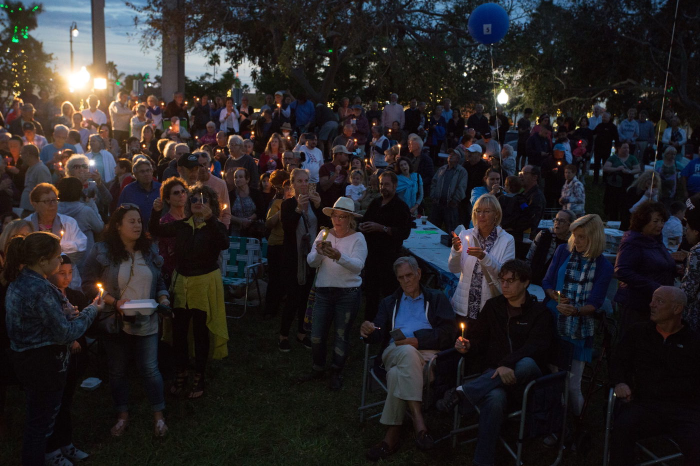 A large crowd holding lit candles at dusk during an outdoor community candlelight vigil